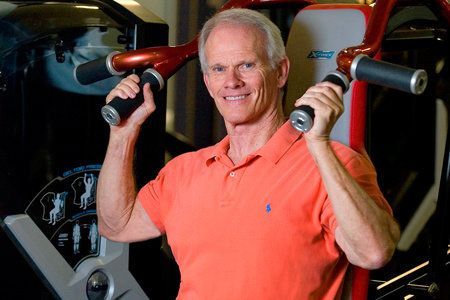 A man in an orange shirt is holding a barbell in a gym.