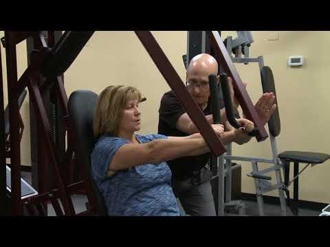 A man is teaching a woman how to use a machine in a gym.