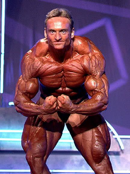 A very muscular man is standing on a stage with his arms crossed.