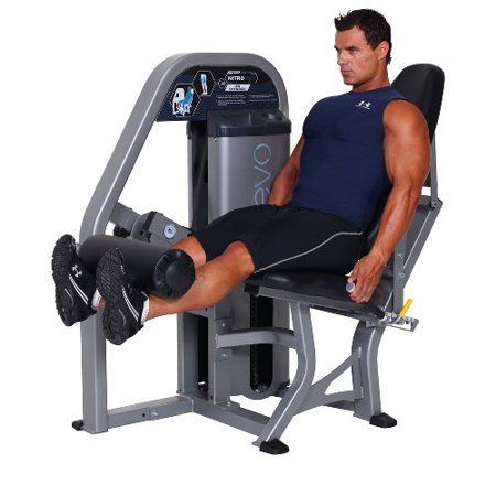 A man is sitting on a leg extension machine in a gym.