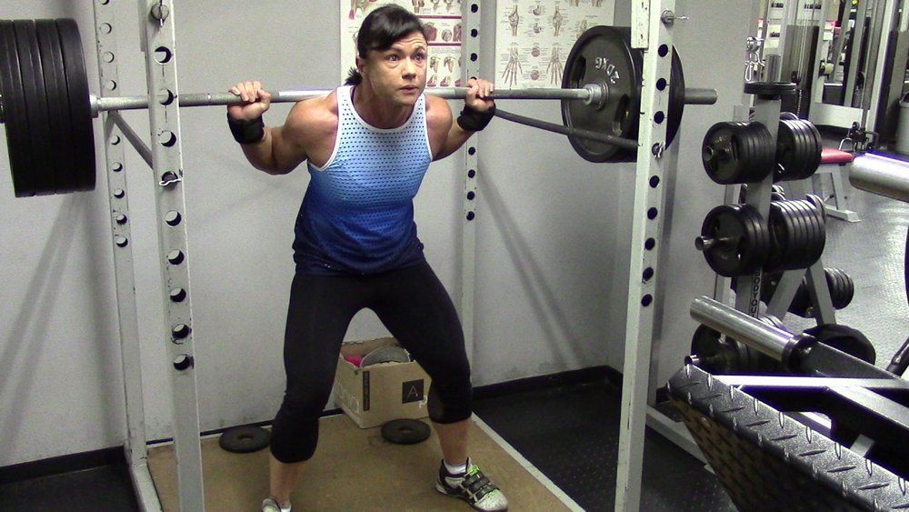 A man is squatting with a barbell in a gym.