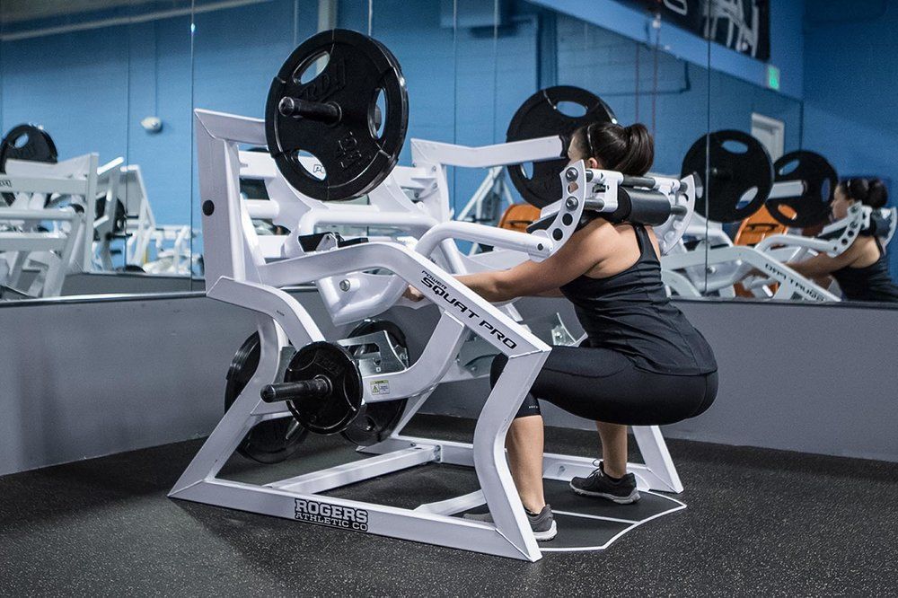 A woman is squatting on a machine in a gym.