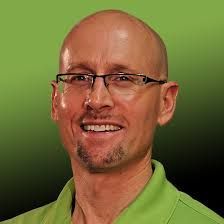 A bald man wearing glasses and a green shirt is smiling.