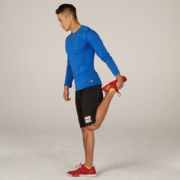 A man in a blue shirt and black shorts is stretching his leg