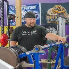 A man is standing next to a barbell in a gym.