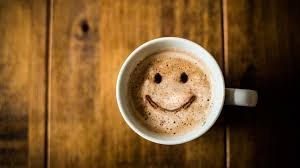 A cup of coffee with a smiley face drawn on it on a wooden table.