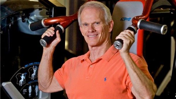 A man in an orange shirt is lifting weights in a gym.