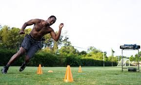 A shirtless man is running through cones on a field.