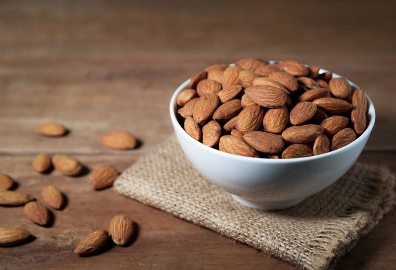 A bowl of almonds is sitting on a wooden table.