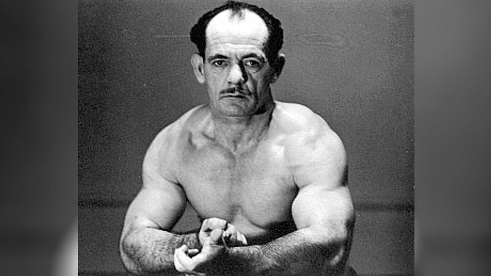 A black and white photo of a shirtless man with his arms crossed.