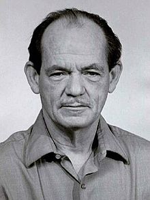 A black and white photo of a man with a mustache wearing a shirt.