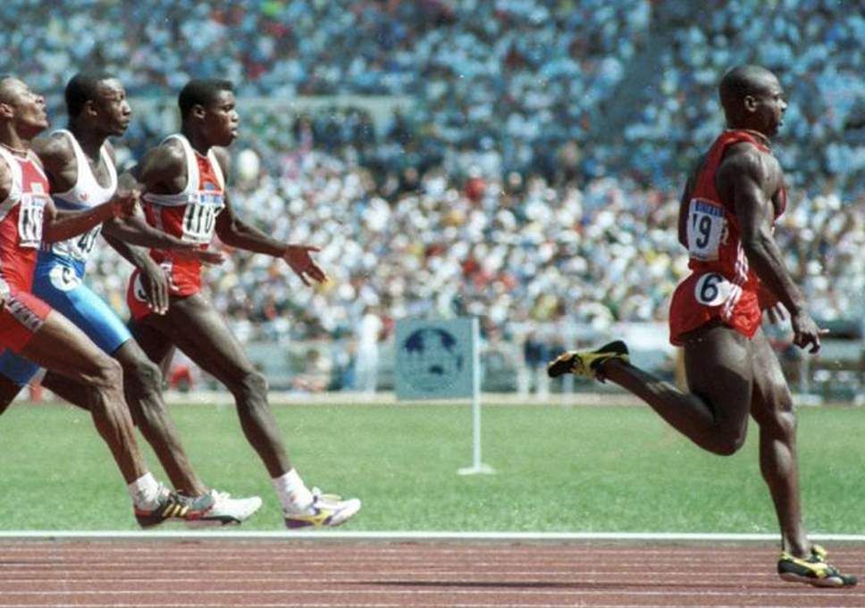 A group of men are running on a track and one of them has the number 6 on his shirt