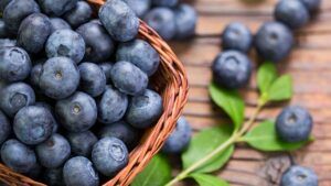 A basket filled with blueberries is sitting on a wooden table.