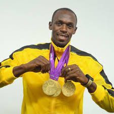 A man in a yellow jacket is holding three gold medals around his neck.