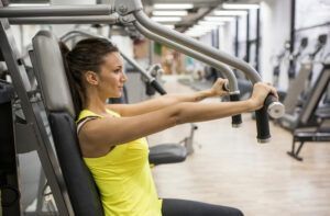 A woman is sitting on a machine in a gym.