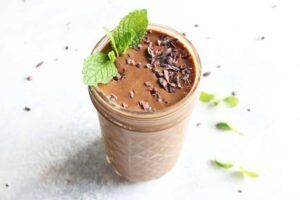 A chocolate smoothie in a mason jar with mint leaves on top.