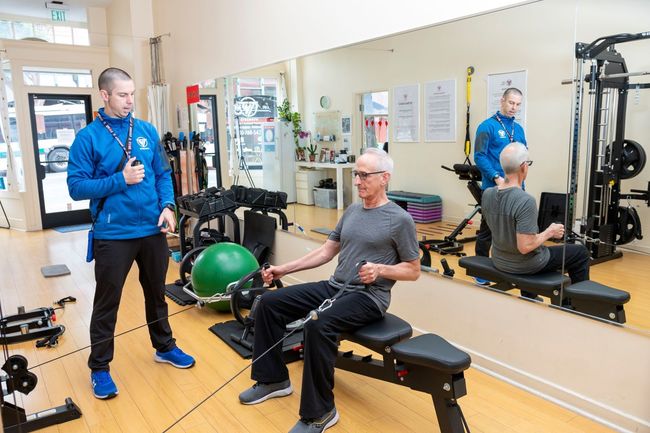 A man is sitting on a bench in a gym while a man stands behind him.