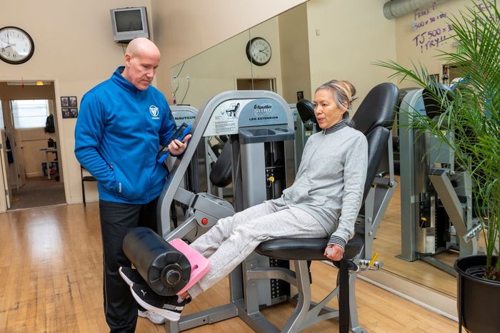 A man is talking to a woman sitting on a machine in a gym.