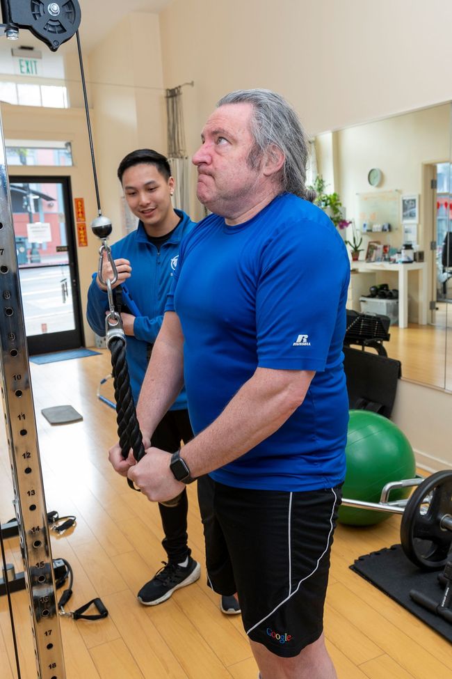 A man in a blue shirt is standing next to another man in a gym.