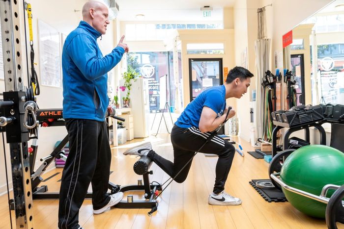 A man is standing next to a man doing squats in a gym.