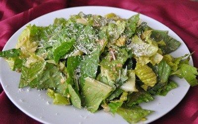 A white plate topped with a salad of lettuce and cheese on a red cloth.