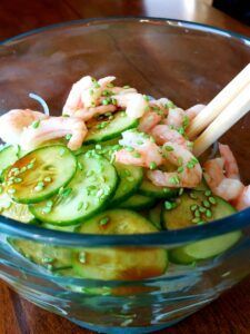 A bowl of shrimp and cucumber salad with chopsticks on a wooden table.