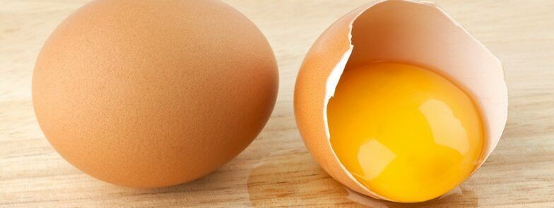 A brown egg and a cracked egg on a wooden table.