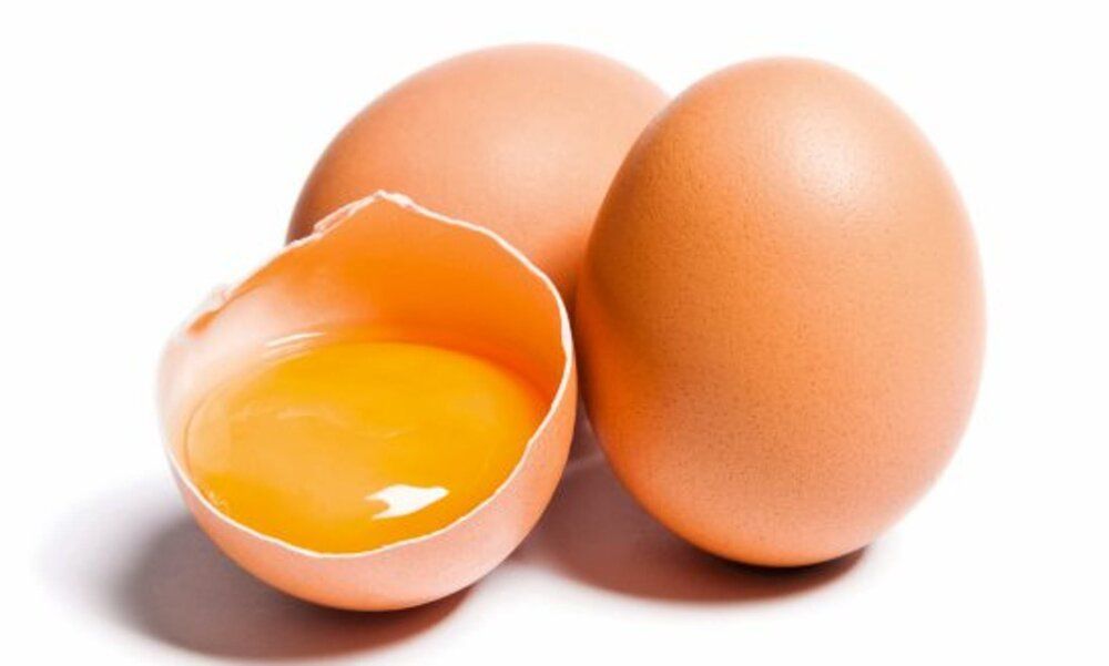 Two brown eggs are sitting next to each other on a white surface . one of the eggs is broken in half.