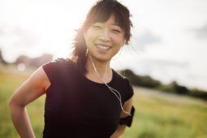 A woman is wearing headphones and smiling while standing in a field.