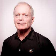 An older man is wearing a black shirt and smiling for the camera.