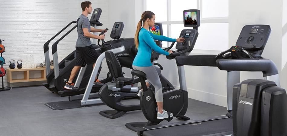 A man and a woman are riding exercise bikes in a gym.