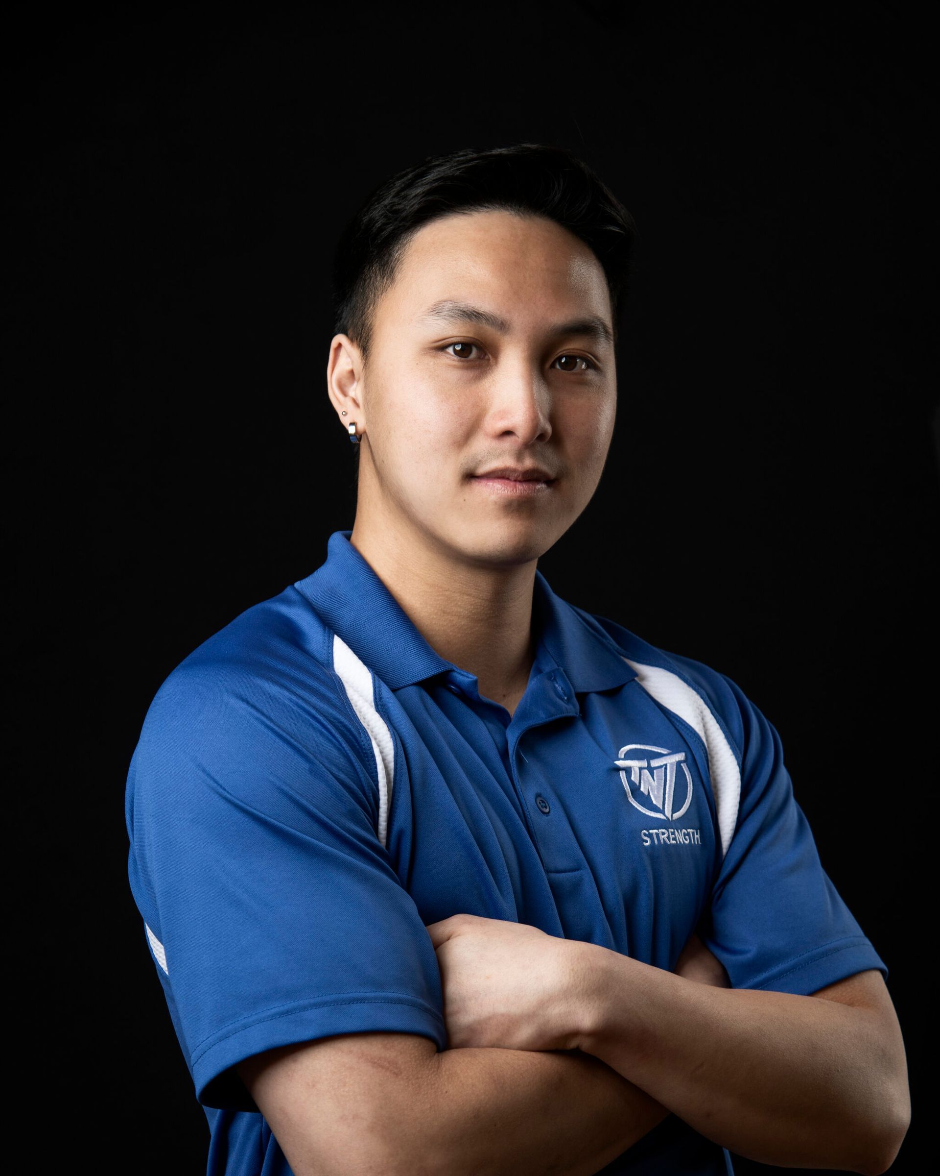 A young man in a blue shirt is standing with his arms crossed.