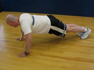 A man is doing push ups with a resistance band around his neck.