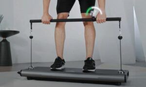 A man is standing on a treadmill holding a bar.