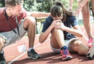 A woman is sitting on the ground with her head in her hands while a man helps her.