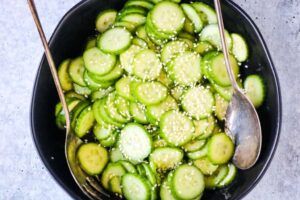 A black bowl filled with sliced cucumbers and spoons.