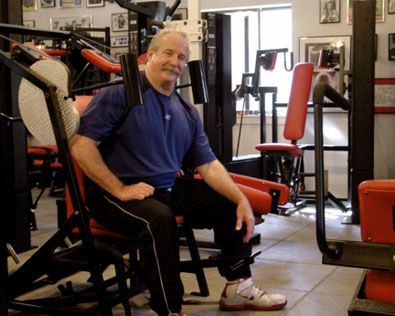 A man in a blue shirt is sitting on a machine in a gym