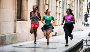 Three women are running down a city sidewalk.