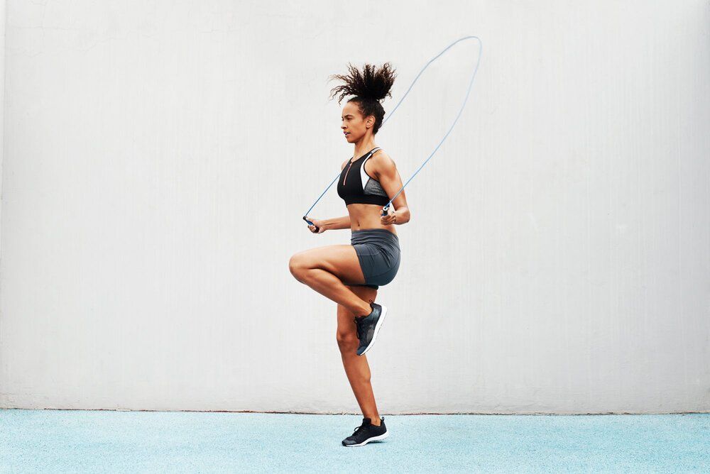 A woman is jumping a jump rope on a blue surface.