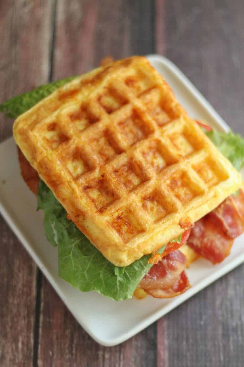 A waffle sandwich with lettuce , bacon and cheese on a white plate.