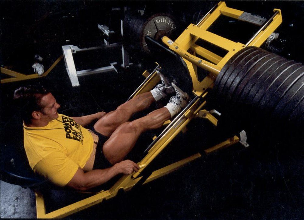 A man in a yellow shirt is using a leg press machine