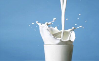 Milk is being poured into a glass on a blue background.