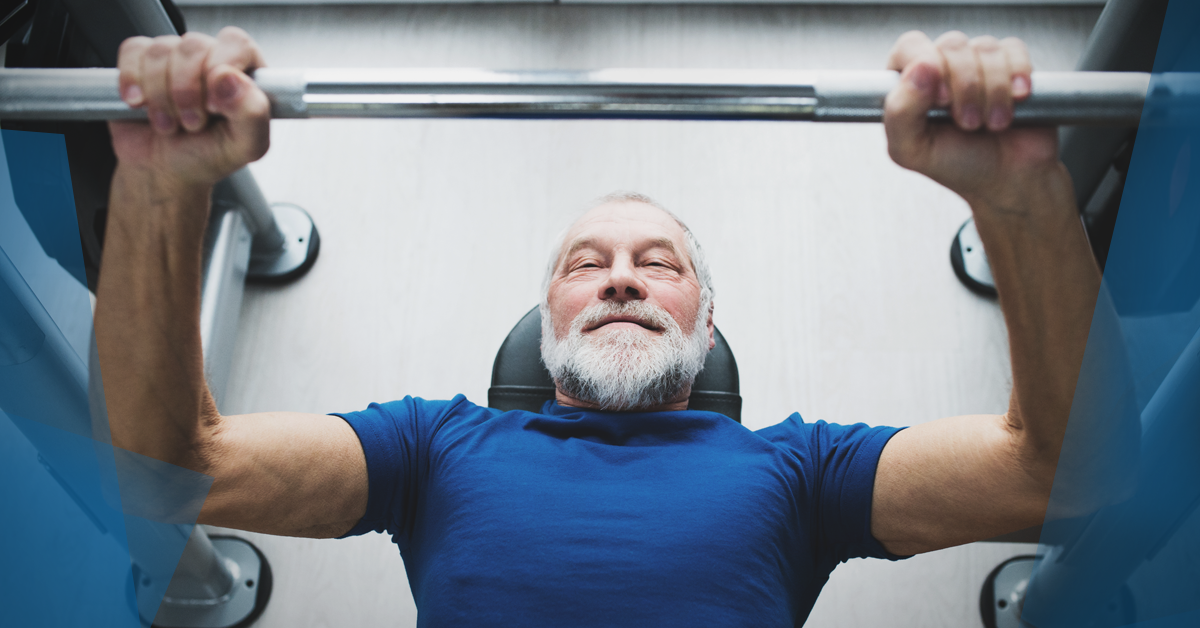 An older man is lifting a barbell on a bench in a gym.