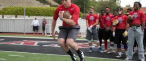 A man in a red shirt is running with a football on a field.