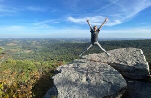 A person is jumping in the air on top of a rock.