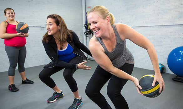 Three women are playing with a medicine ball in a gym.