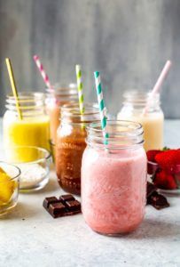 A variety of milkshakes in mason jars with straws on a table.