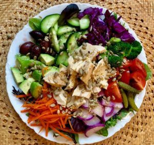 A white plate topped with a salad of vegetables and chicken