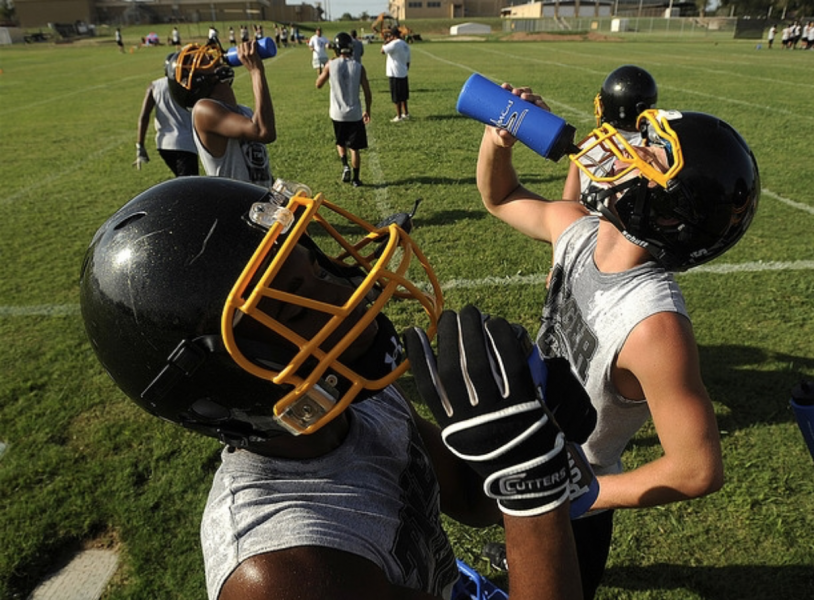 A football player is drinking water from a blue bottle