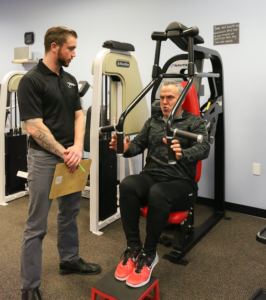 A man is talking to a man on a machine in a gym